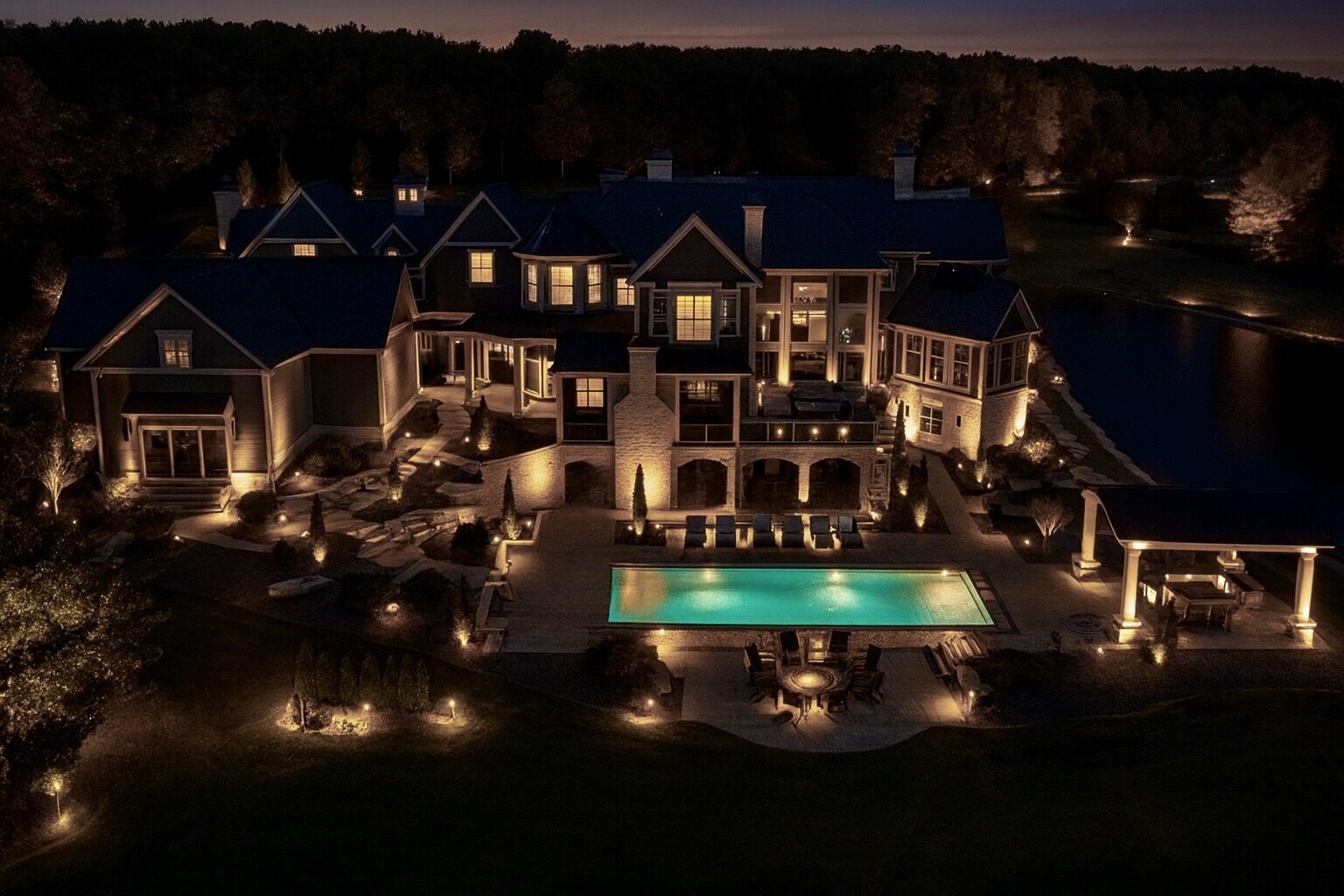 Luxury estate at twilight with architectural uplighting, lit pool and landscape lighting
