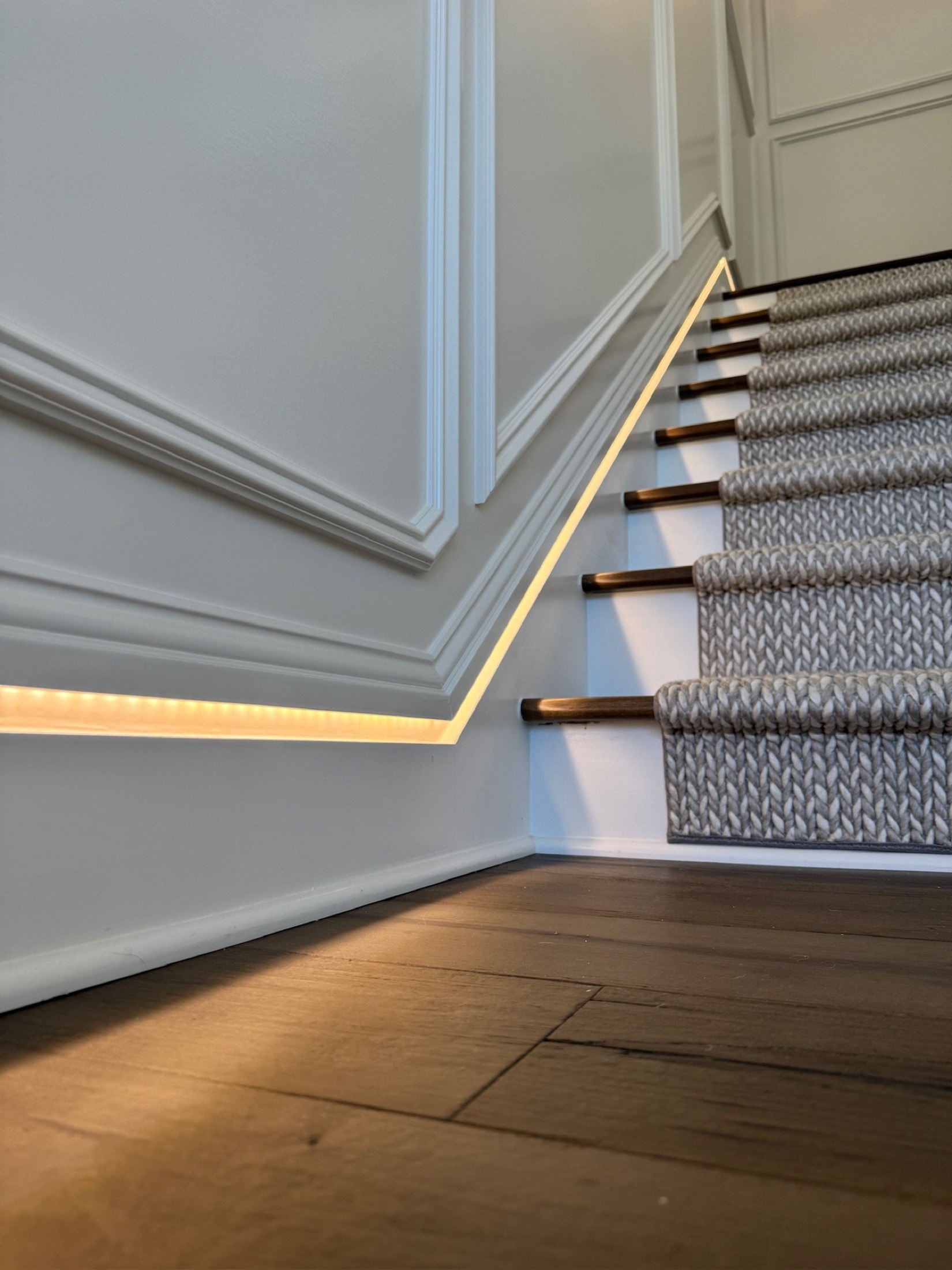 Warm tunable cove lighting glowing along wainscoting beside a carpeted staircase