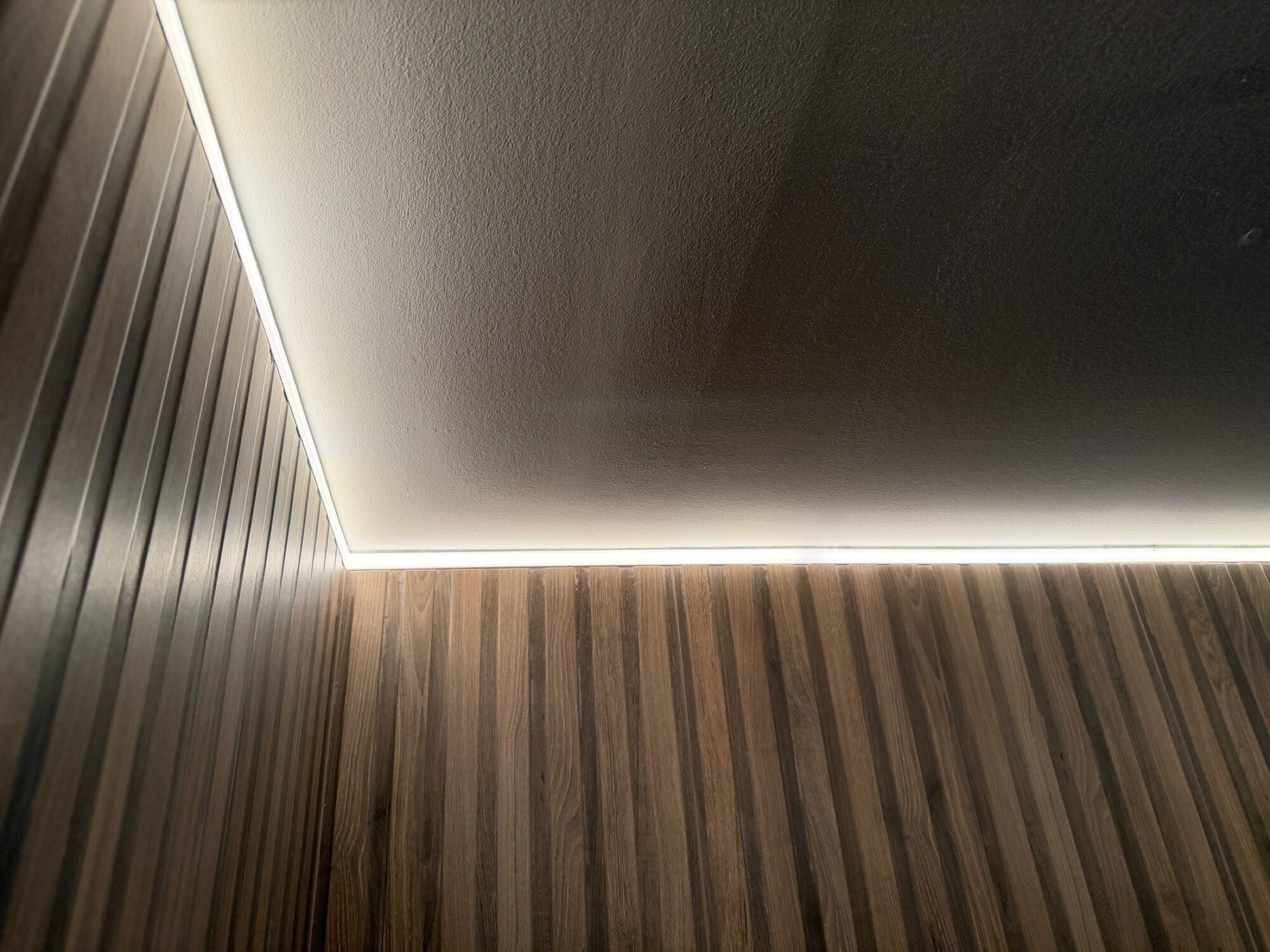 Dimmable LED cove lighting along a ceiling edge above vertical wood slat walls