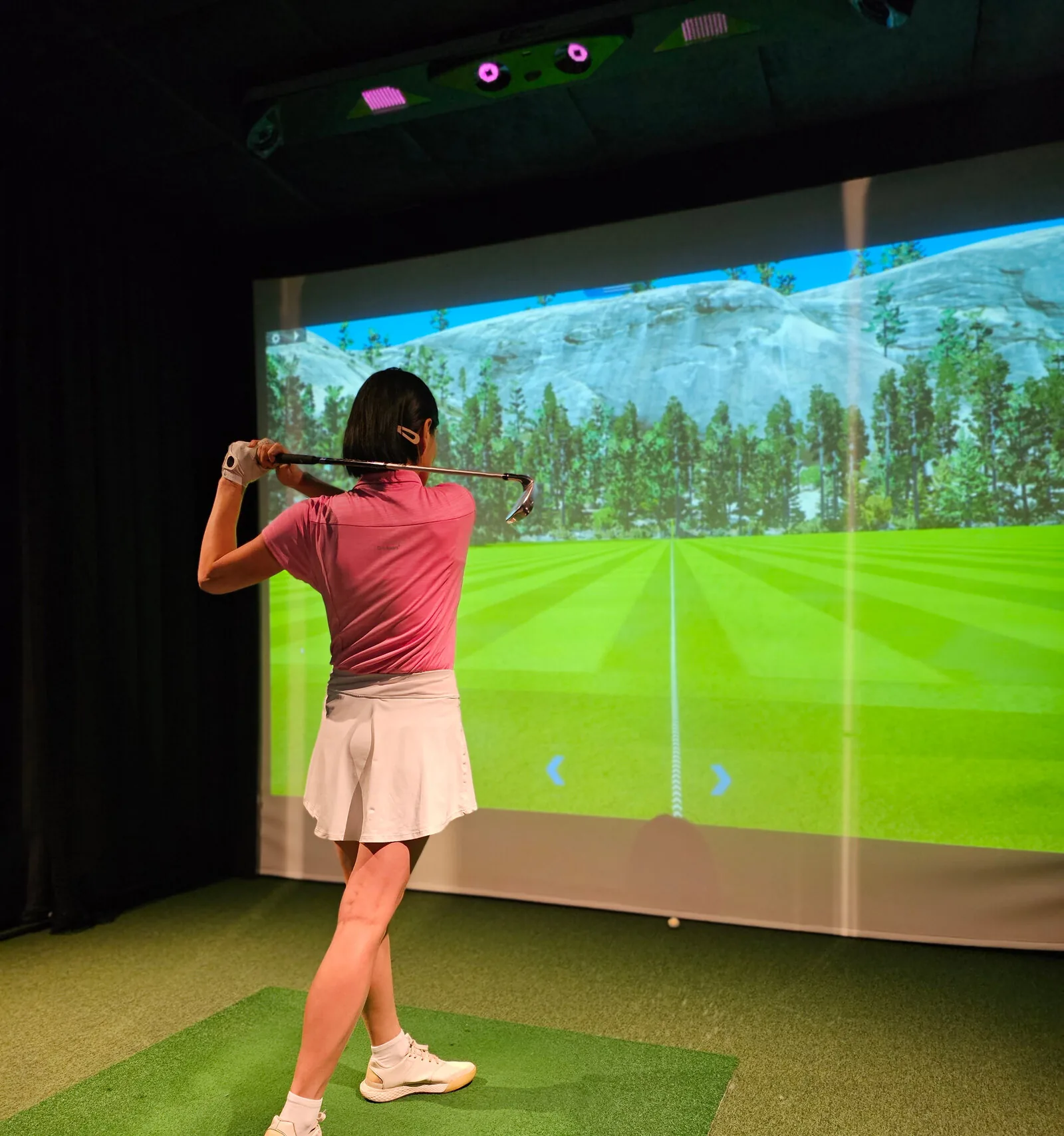 Golfer mid-swing in front of a golf simulator projection screen in a dedicated room