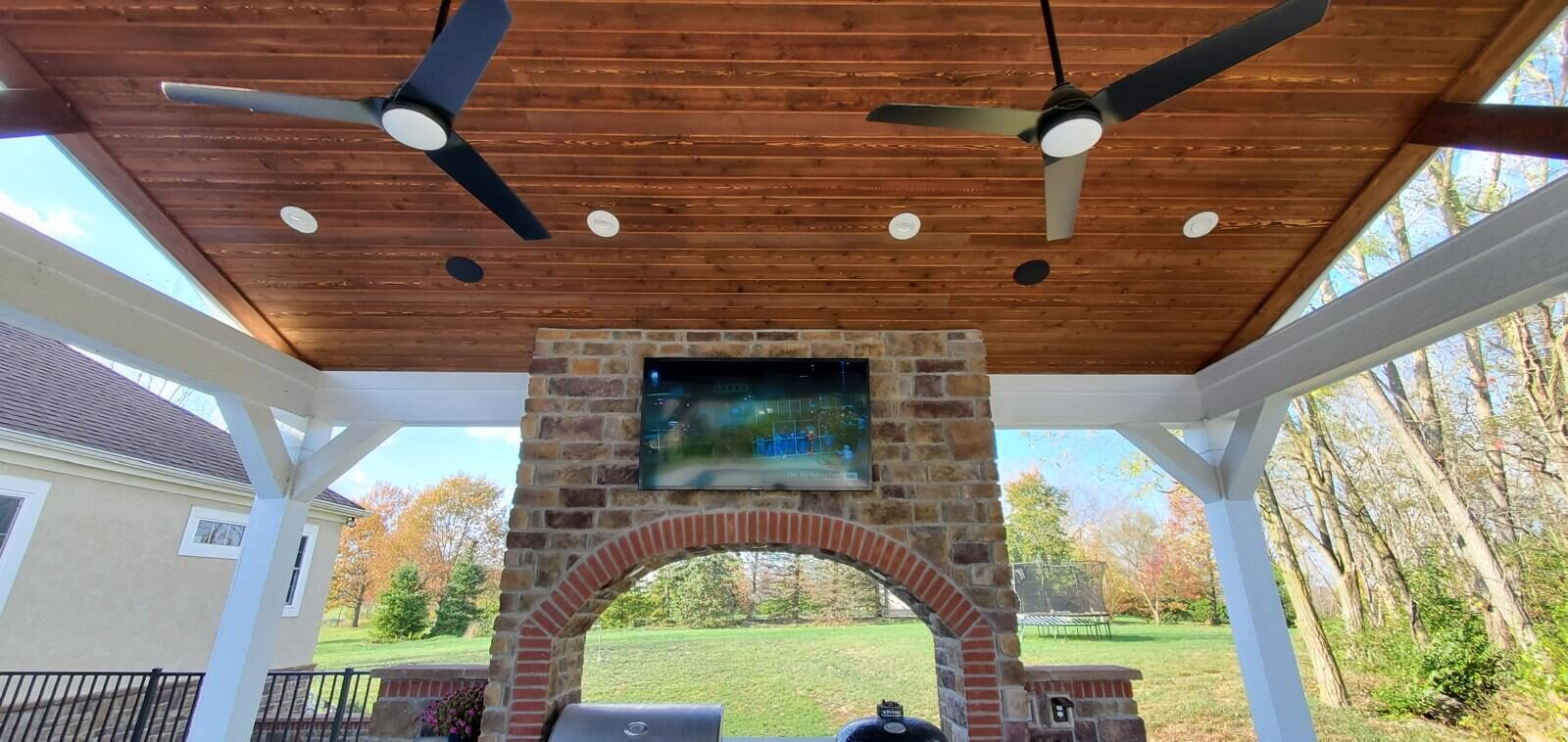 Covered patio pavilion with an outdoor TV over a stone fireplace and in-ceiling speakers, Granville OH